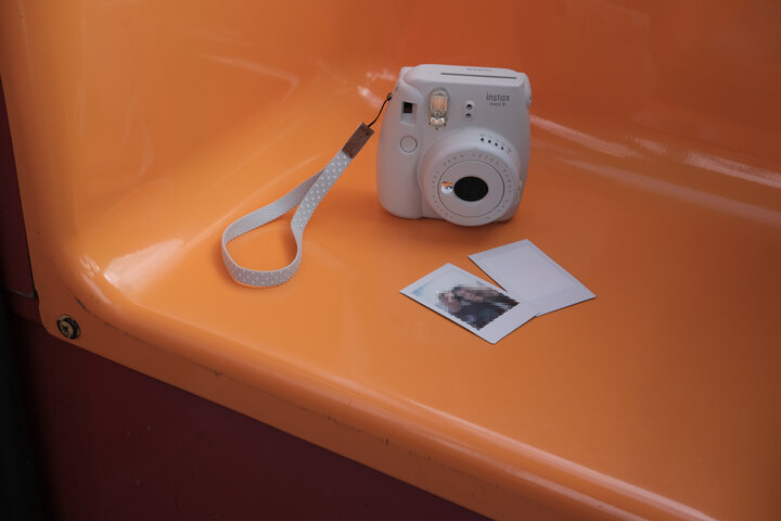 A polaroid type camera and two developing images sitting on a bench