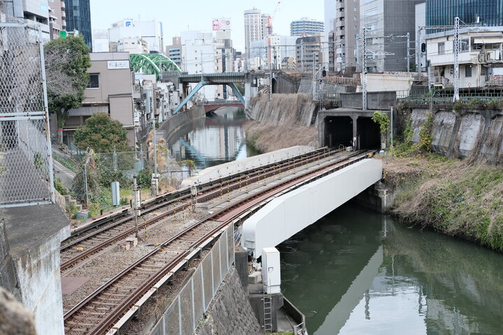 A tunnel with two train tracks opening over a river